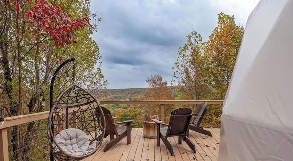 Een houten terras met een hangstoel, twee stoelen en een bijzettafeltje.