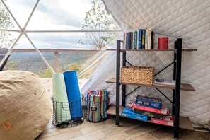 A room with a large window, a bookshelf, yoga mats, and board games.