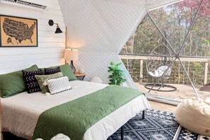Een gezellige slaapkamer met een bed, kussens, een lamp, een plant en een stoel.