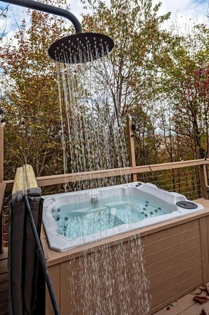 Een hottub met douchetje, omringd door een houten terras en bomen.