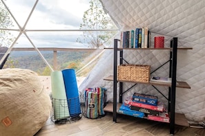 Una habitación con un ventanal grande, una estantería, tapetes de yoga y juegos de mesa.