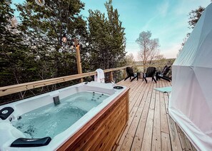 A wooden deck with a hot tub, outdoor seating, and a tent.