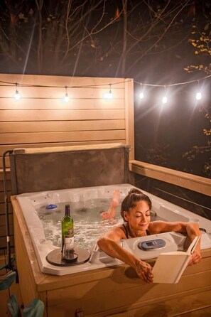 Una bañera de hidromasaje con panel digital, una botella y una persona leyendo un libro.