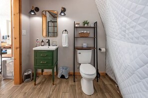 Un baño con tocador verde, inodoro blanco, espejo y estante con artículos de aseo.