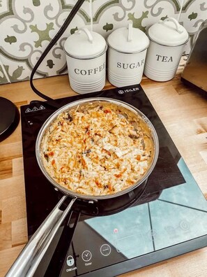 A kitchen with a pan on an induction cooktop, three labeled containers (coffee, sugar, tea), and a patterned backsplash.