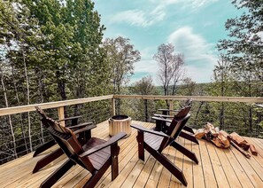 Una terraza de madera con dos sillas Adirondack, una mesa redonda y un brasero.