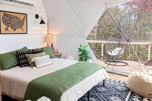 A cozy bedroom with a bed, pillows, a lamp, a plant, and a chair.