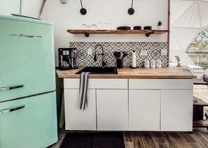 Una cocina compacta con un refrigerador verde azulado antiguo, una encimera de madera y un salpicadero con diseño.