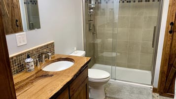 Ein Badezimmer mit einem Holzkosmetikschrank, einem weißen Waschbecken, einer Toilette und einer Duschkabine.