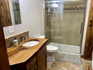 Un baño con tocador de madera, lavamanos blanco, inodoro y cabina de ducha con paredes de vidrio.