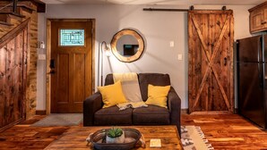 A cozy living room with a wooden door, a round mirror, a sofa with cushions, and a coffee table with a plant.