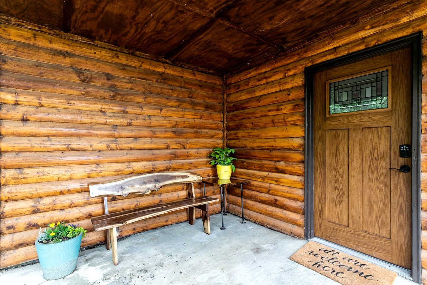 A wooden cabin with a bench, a potted plant, a door, and a welcome mat.