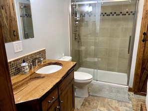 Un baño con tocador de madera, lavamanos blanco, inodoro y cabina de ducha con paredes de vidrio.