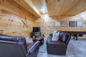 L'interno di una baita in legno con un divano in pelle, una televisione e quadri appesi al muro.