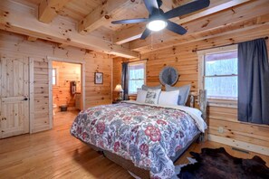 A wooden cabin bedroom with a bed, ceiling fan, and windows.