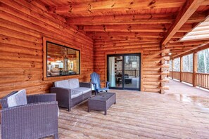 A log cabin with a covered porch, wicker furniture, and a sliding glass door leading to an outdoor area.