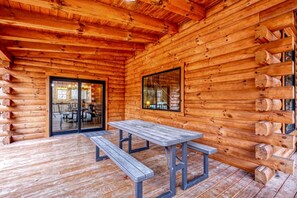 Una cabaña de madera con una mesa y bancos de madera, una puerta de vidrio que da a un comedor interior, y una ventana con vistas al exterior.