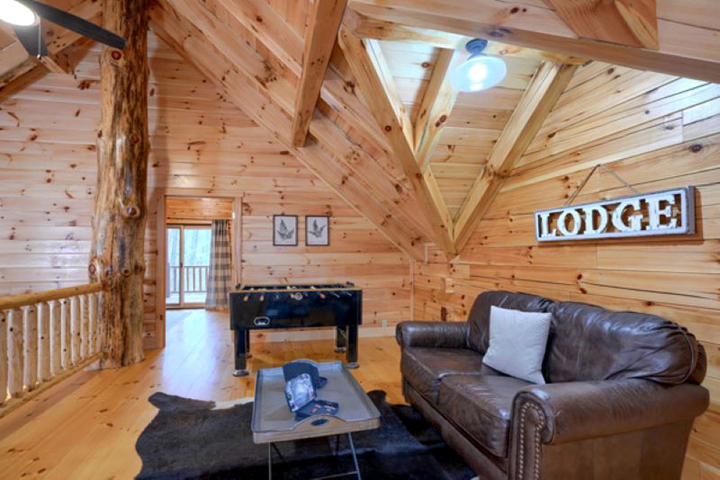 A wooden lodge interior with a sofa, a foosball table, and a sign that reads 'LODGUE'.