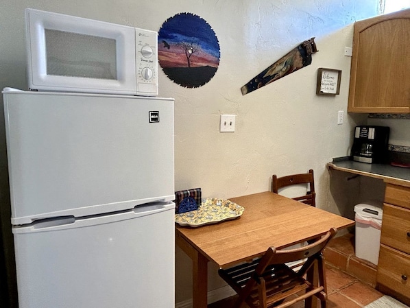 Una cucina compatta con frigorifero, microonde, tavolo in legno, sedie e un piccolo armadietto.