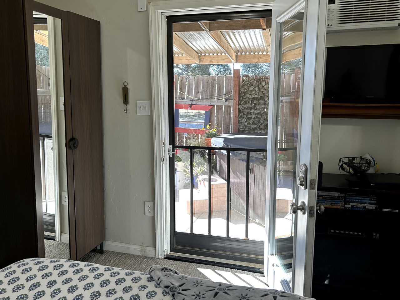 Una habitación con puerta de vidrio corredera que da a un espacio exterior, una cama con ropa de cama estampada y un televisor sobre un mueble.