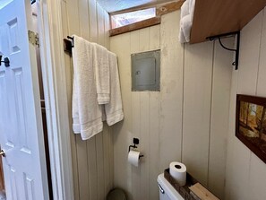 Ein Badezimmer mit Holzwänden, einer Toilette, einem Handtuchhalter und einem Fenster.