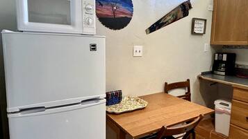 Una cocina compacta con refrigerador, microondas, mesa de madera, sillas y un mueble pequeño.