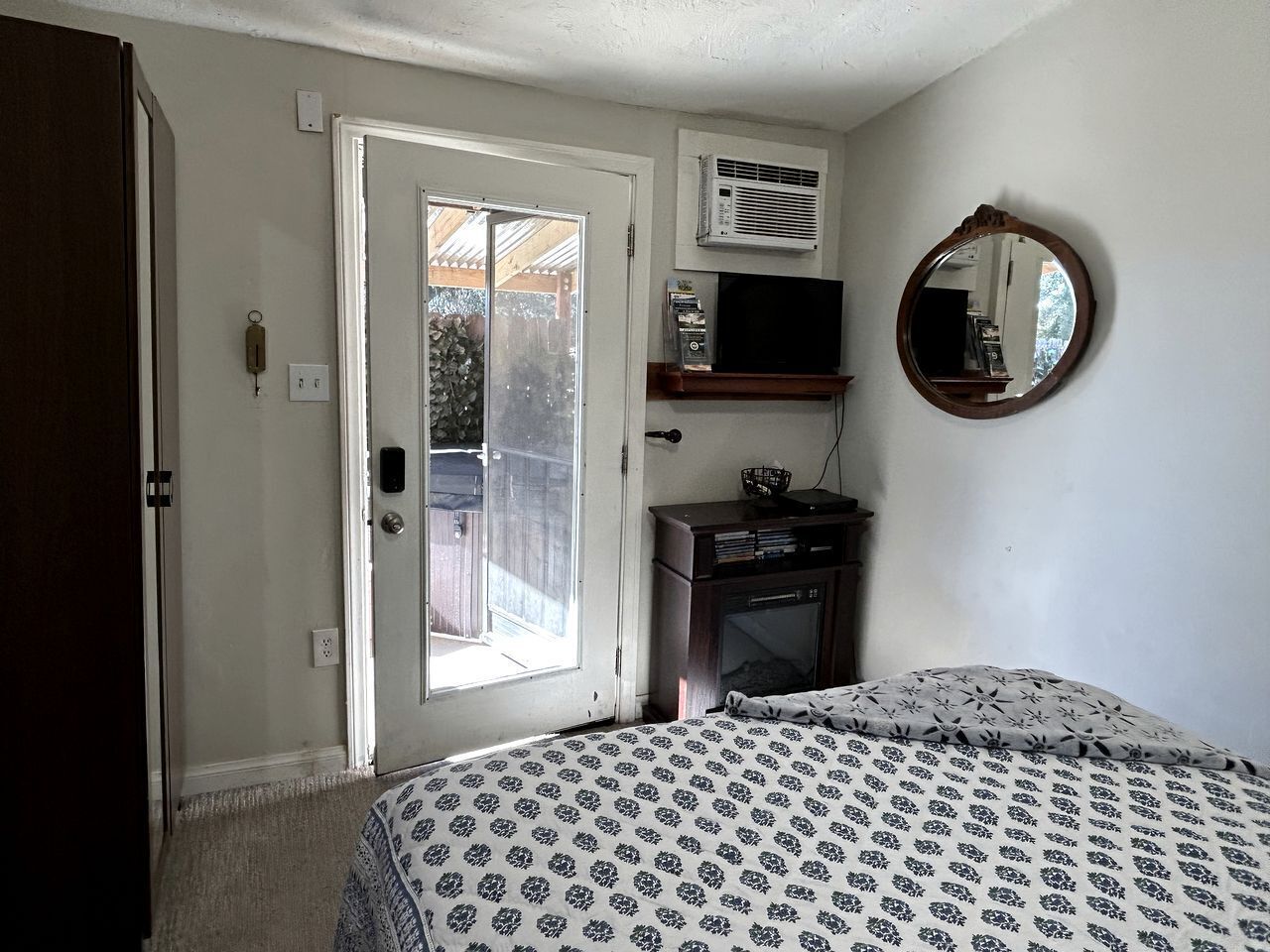 Een slaapkamer met een bed, een dressoir, een spiegel en een deur naar een buitenruimte.