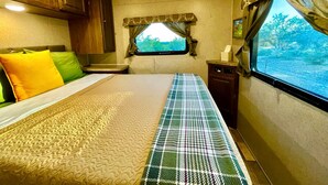 A bedroom with a bed, a window with curtains, a small table, and a cabinet.