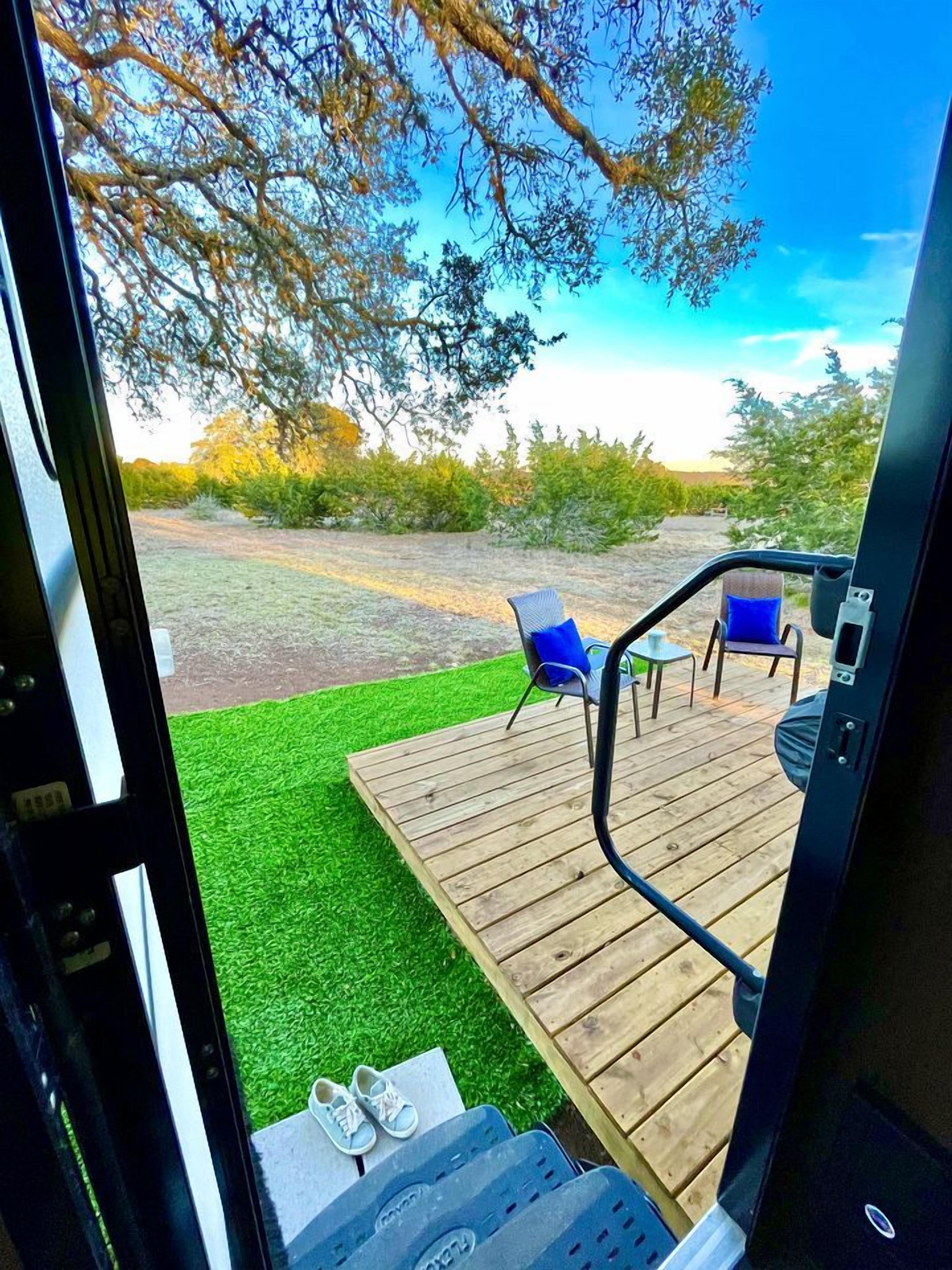 A deck with chairs and a table, a grassy area, and trees in the background.