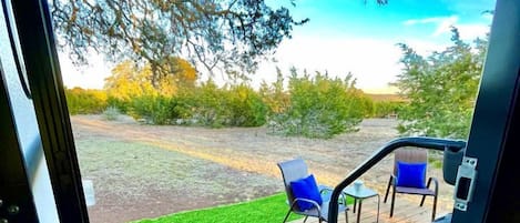 A deck with chairs and a table, a grassy area, and trees in the background.