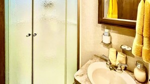 A bathroom with a glass shower enclosure, a sink with a mirror, and towels.