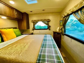 A bedroom with a bed, a window with curtains, a small table, and a cabinet.