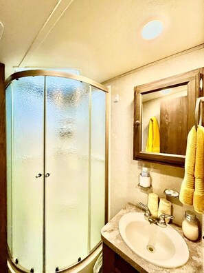 A bathroom with a glass shower enclosure, a sink with a mirror, and towels.