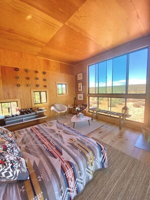 Une chambre spacieuse avec un grand lit, un bureau, une chaise et une vue sur le désert grâce à de grandes fenêtres.