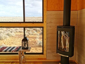 A room with a large window, a wooden bench, a lantern, and a wood-burning stove. - Modern Cubed Cabin Accommodation for a Getaway near the Grand Canyon, Arizona (Page)