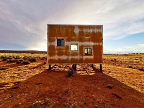 Edificio de una planta con dos ventanas, en un paisaje árido.