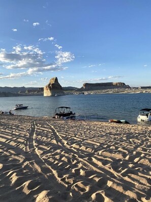 Une plage de sable avec des bateaux, une formation rocheuse dans l’eau et un ciel dégagé.