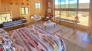 Ein geräumiges Schlafzimmer mit einem großen Bett, einem Schreibtisch, einem Sessel und Blick auf die Wüste durch große Fenster.
