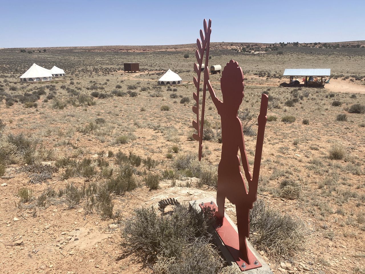 Paisagem desértica com tendas e uma grande escultura vermelha.