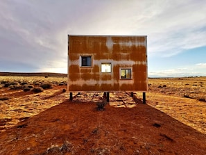 Un bâtiment d’un seul étage, doté de deux fenêtres, situé dans un paysage désolé.