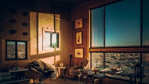 Ein gemütliches Zimmer mit großem Fenster, einem Bett, einem Sessel, einem kleinen Tisch und einer Gitarre.