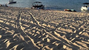Ein sandiger Strand mit Booten, eine Felsformation im Wasser und ein klarer Himmel.