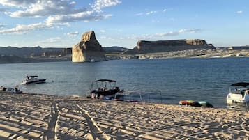 A sandy beach with boats, a rocky formation in the water, and a clear sky.