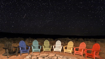 A row of Adirondack chairs arranged around a stone fire pit under a starry night sky.