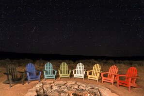 A row of Adirondack chairs arranged around a stone fire pit under a starry night sky. - Modern Cubed Cabin Accommodation for a Getaway near the Grand Canyon, Arizona (Page)