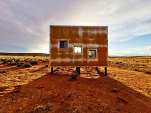 Un bâtiment d’un seul étage, doté de deux fenêtres, situé dans un paysage désolé.