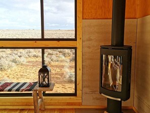 A room with a large window, a wooden bench, a lantern, and a wood-burning stove. - Modern Cubed Cabin Accommodation for a Getaway near the Grand Canyon, Arizona (Page)