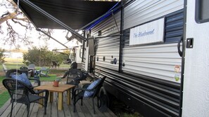 A covered outdoor area with a dining table and chairs, a sign reading 'The Bluebonnet,' and a trailer with a metal exterior.