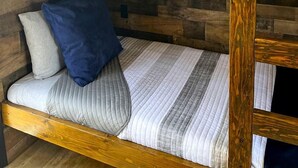 A bunk bed with a wooden headboard, a wall-mounted sign spelling 'DOZY,' and a wooden wall paneling.