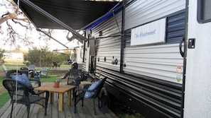 A covered outdoor area with a dining table and chairs, a sign reading 'The Bluebonnet,' and a trailer with a metal exterior.